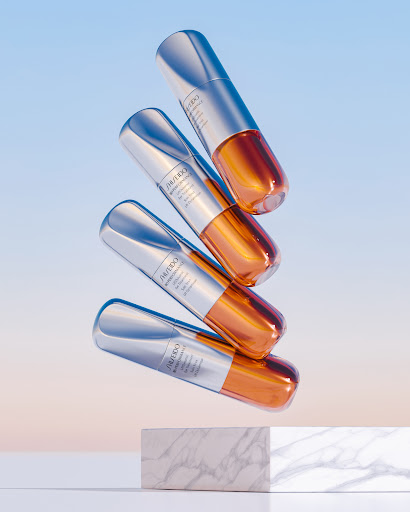 Beauty product still life: Four Shiseido serum bottles stacked in a studio setting with a marble block against a gradient sky blue background.