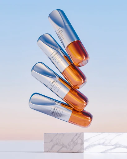 Beauty product still life: Four Shiseido serum bottles stacked in a studio setting with a marble block against a gradient sky blue background.