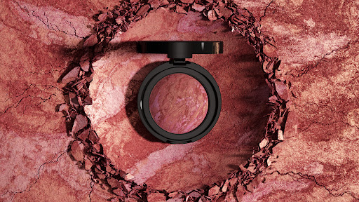 Overhead shot of face blush compact in black case on a textured earth-toned background with cracked rock and loose rock pieces.