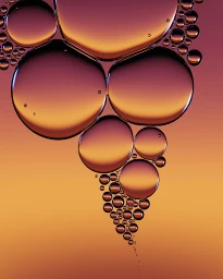Close-up macro shot of spherical oil droplets floating and clustering against a warm gradient background in amber and purple tones.