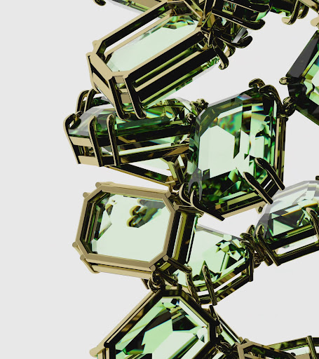 Close-up of a geometric jewelry design featuring gold metal framework surrounding light green gemstones, set against a plain, light background.