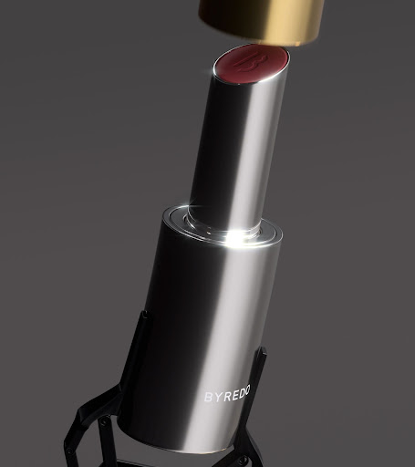 Close-up studio shot of BYREDO lipstick on a black display stand, highlighting its metallic case and deep-red hue.