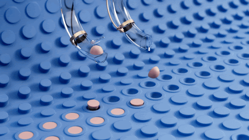 Close-up of robotic arms placing pills into a blue surface with circular indentations in a high-tech or pharmaceutical environment.