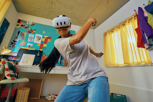 Woman in VR headset in casual home setting, interacting with virtual reality. Person is in jeans, t-shirt, with desk and decor behind.