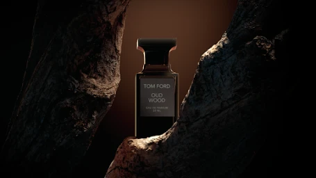 Tom Ford Oud Wood perfume bottle framed between two textured tree bark sections in dramatic lighting