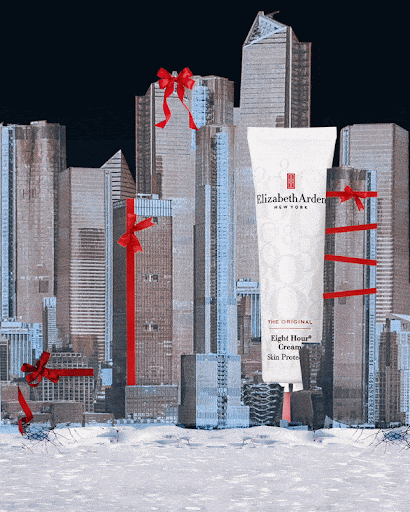Elizabeth Arden Eight Hour Cream stands tall in a city of skyscrapers adorned with festive red bows, set against a dark sky and snow.