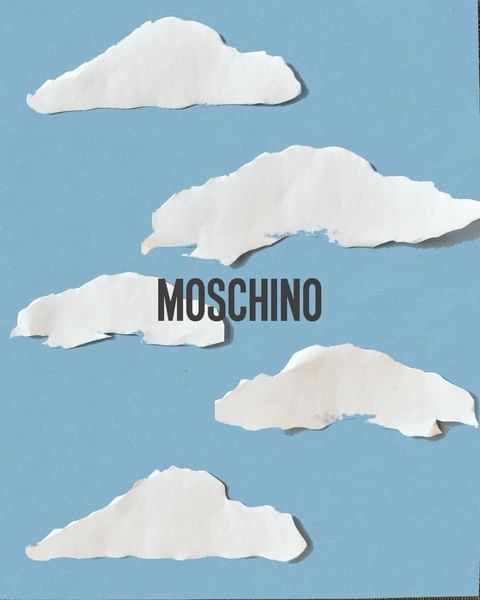Stylized shot of paper clouds on a blue background with the brand name MOSCHINO in the center, creating a whimsical fashion aesthetic.