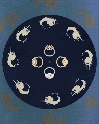 Overhead shot of four diamond rings in gold and silver tones, displayed on a dark blue surface with stylized eye shapes pattern.
