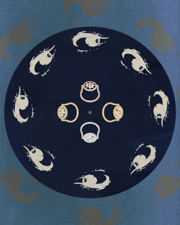 Overhead shot of four diamond rings in gold and silver tones, displayed on a dark blue surface with stylized eye shapes pattern.