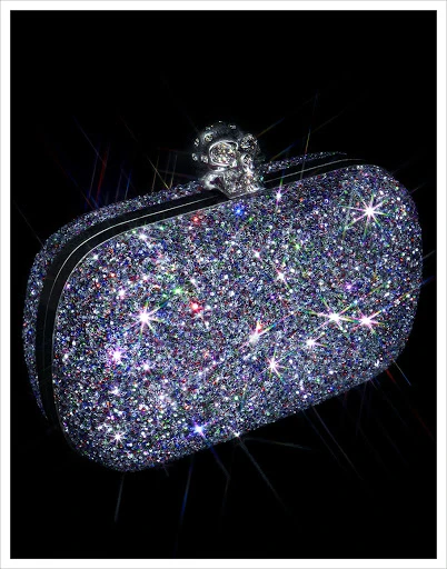 Sparkling clutch bag with a jeweled skull clasp against a black background. A fashionable accessory for evening wear or special occasions.