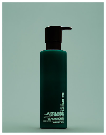 Dark green Shu Uemura Ultimate Remedy bottle with black pump on an aqua backdrop in portrait orientation, beauty and haircare.