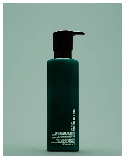 Dark green Shu Uemura Ultimate Remedy bottle with black pump on an aqua backdrop in portrait orientation, beauty and haircare.