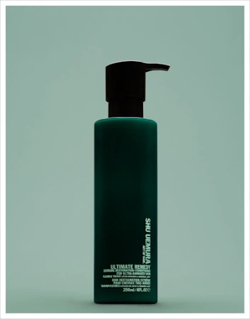 Dark green Shu Uemura Ultimate Remedy bottle with black pump on an aqua backdrop in portrait orientation, beauty and haircare.