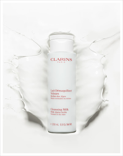 Clarins Cleansing Milk product shot. White bottle of Clarins Lait Démaquillant Velours surrounded by splash of white liquid.
