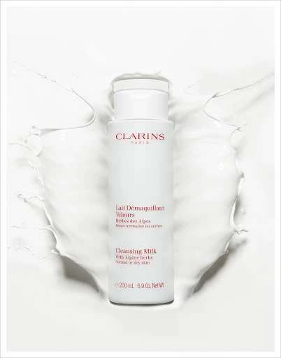 Clarins Cleansing Milk product shot. White bottle of Clarins Lait Démaquillant Velours surrounded by splash of white liquid.