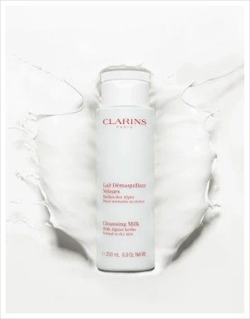 Clarins Cleansing Milk product shot. White bottle of Clarins Lait Démaquillant Velours surrounded by splash of white liquid.