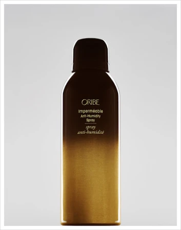 Oribe Impermeable Anti-Humidity Spray bottle with a brown top fading into a gold bottom on a neutral grey background.