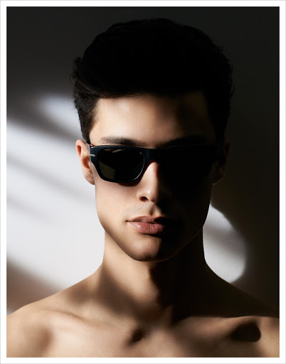 Portrait of a man wearing dark sunglasses against a light background with dramatic shadows by photographer Kutlu