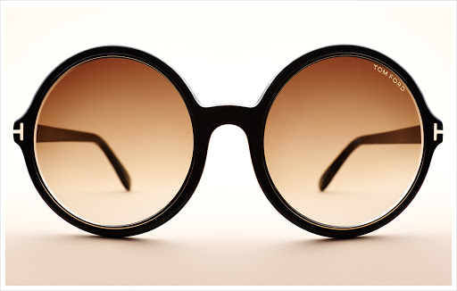 Close-up of round sunglasses with a brown gradient lens and black frames, showcasing the 'Tom Ford' brand on a white background.