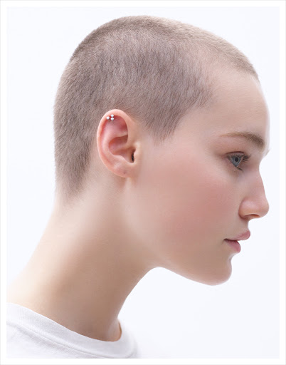 Profile portrait of a young adult woman with a shaved head against a bright white background, showcasing a minimalist and clean aesthetic.