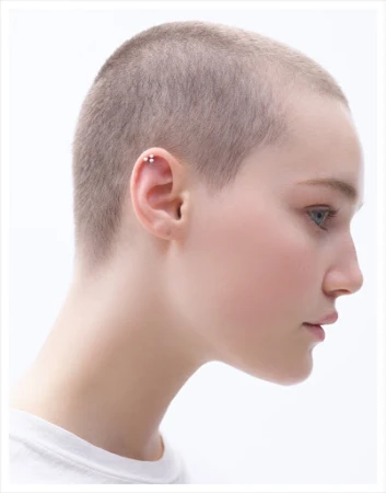 Profile portrait of a young adult woman with a shaved head against a bright white background, showcasing a minimalist and clean aesthetic.