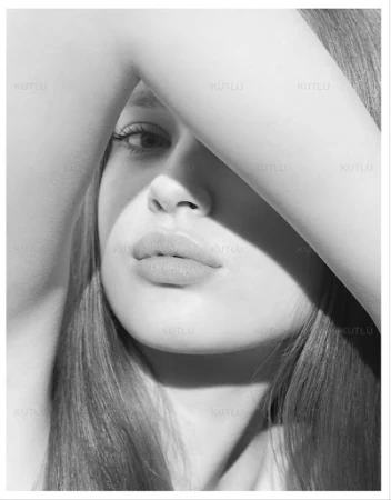 Monochrome portrait of a woman with her arm raised across her face, casting sharp diagonal shadows across her features.