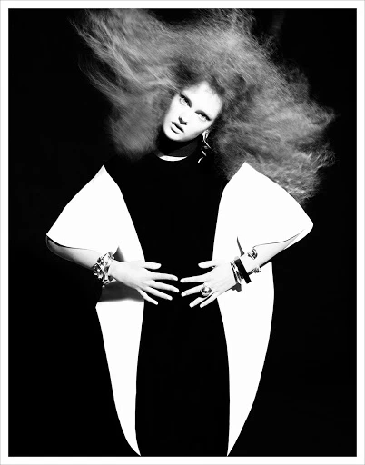 Fashion photo in black and white. Woman with voluminous hair poses in a black and white dress with dramatic flared sleeves and jewelry.