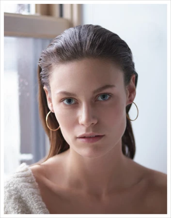 Portrait of a woman with slicked-back dark hair wearing gold hoop earrings by photographer Kutlu