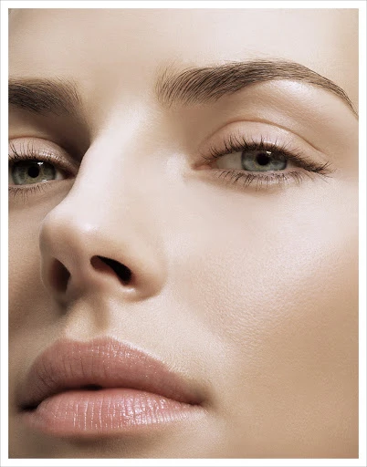 Close-up studio shot of a woman's face, highlighting soft skin, pronounced eyebrows, and eyes, captured in a beauty and fashion context.