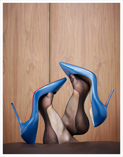 Elevated studio shot of adult female feet in sheer black stockings inside blue leather high heel shoes with a wood background.