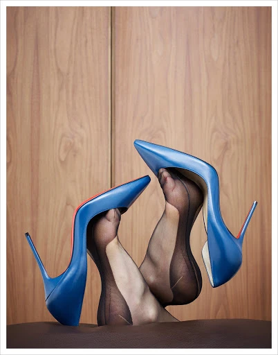 Elevated studio shot of adult female feet in sheer black stockings inside blue leather high heel shoes with a wood background.