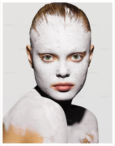 Close-up portrait of a woman with a facial mask, featuring smooth skin, direct eye contact, and a clean, light grey background.