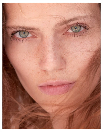 Close-up portrait of a redhead woman with green eyes and freckles, capturing her natural beauty in a photo studio setting.