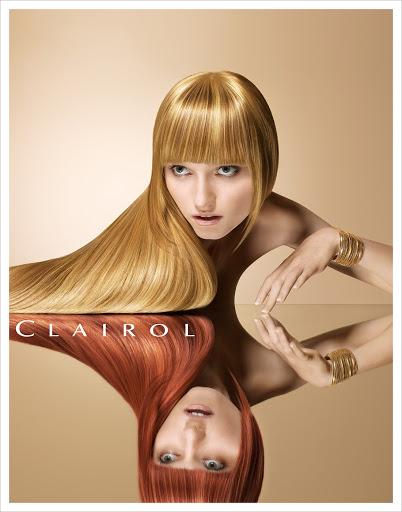 Woman with blonde hair poses with a reflection showing red hair, with gold bangle bracelets on a beige background in a beauty ad.