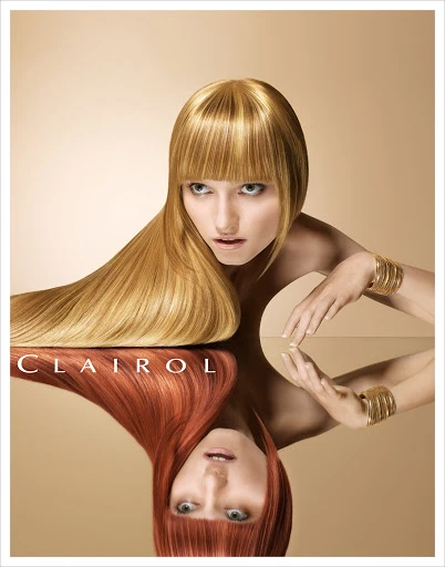 Woman with blonde hair poses with a reflection showing red hair, with gold bangle bracelets on a beige background in a beauty ad.