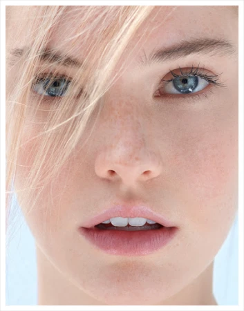 Extreme close up portrait of a young woman with blue eyes, light freckles, and blonde hair strands falling across her face.
