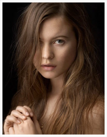 Close-up portrait of a young woman with long wavy brown hair falling across her face, captured by photographer Kutlu.