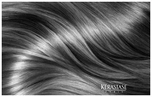 Close-up black and white shot of shiny wavy human hair, promoting Kérastase Paris brand with its logo visible at the bottom of the frame.