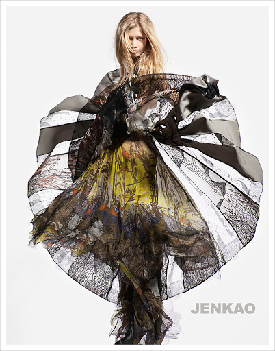 Fashion shot of a fair-skinned model in a large multi-colored dress against a white background in a studio with soft, diffused lighting.