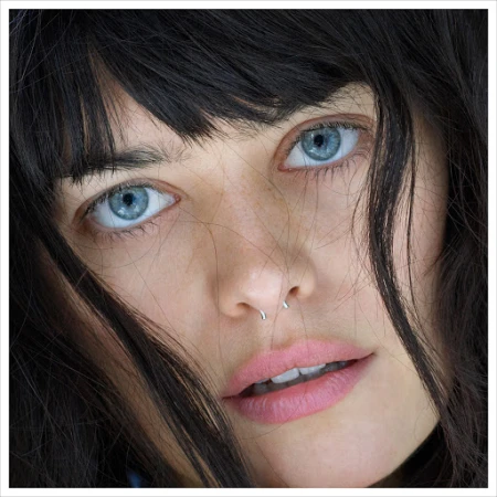 Close-up portrait of a woman with dark hair, striking blue eyes, and a silver septum ring photographed by Kutlu