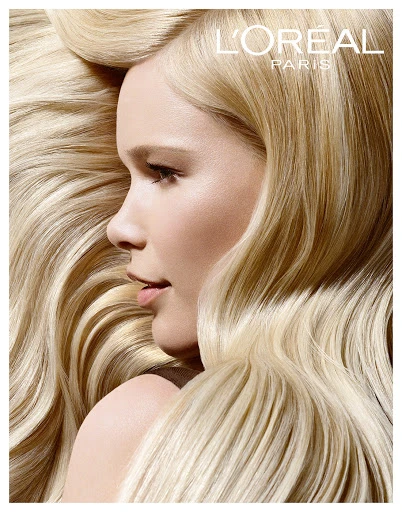 Close-up profile of a fair-skinned adult female with blonde wavy hair, fair skin, and a shoulder visible against a golden background.
