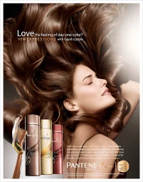 Woman with flowing brown hair lying down beside three shampoo bottles in a commercial beauty advertisement.