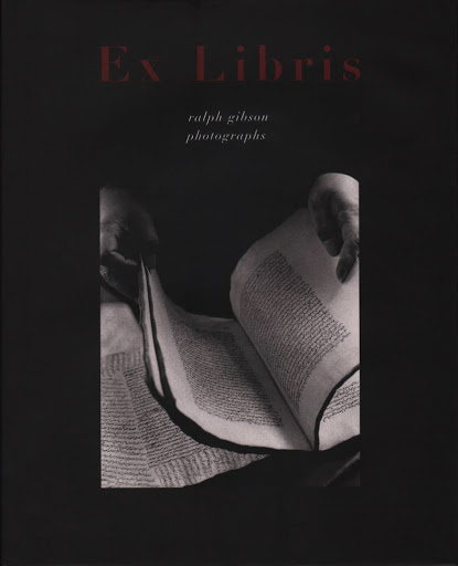 Monochrome book cover featuring hands holding open a heavy medieval manuscript with dense handwritten text under red title lettering.