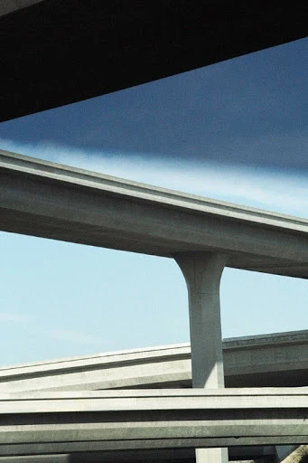 Concrete overpass system with multiple layers and supports against a light blue sky, creating an infrastructure network.