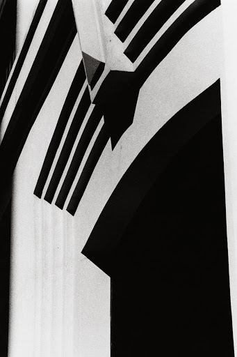 Monochromatic abstract architectural image of black and white stripes converging towards an arched entryway with deep contrasting shadows.