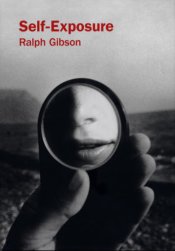 Black and white photograph of a hand holding a mirror reflecting a face, with a blurred landscape background and text on top.