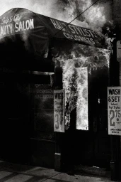 Monochrome street-level photograph of a beauty salon storefront with an awning and signage displaying text.