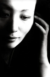 Close-up monochrome portrait of a woman with her hand near her face under dramatic low-key lighting by photographer Ralph Gibson.