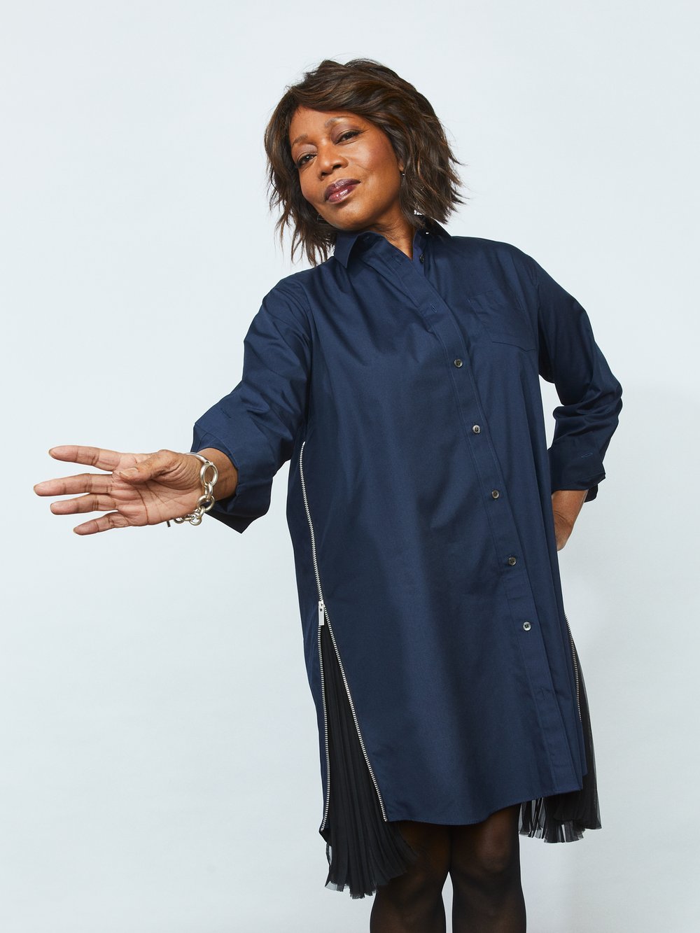 Elegant Black woman in a navy-blue shirt dress with a side zipper, accented by a silver bracelet, posing confidently against a white backdrop.