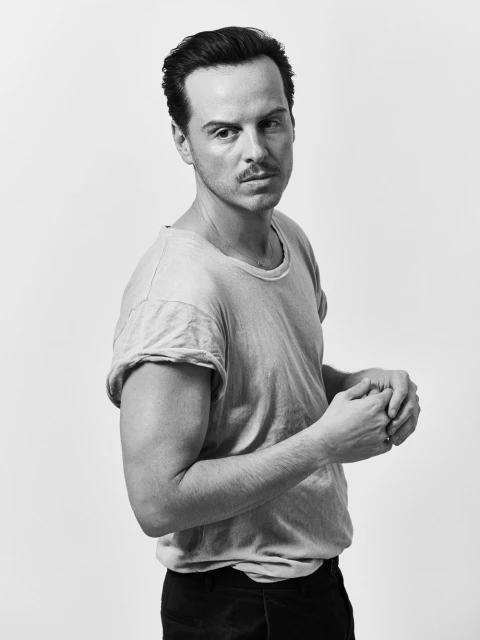 Black and white portrait of a man with dark hair and a moustache, wearing a light t-shirt, against a plain background.